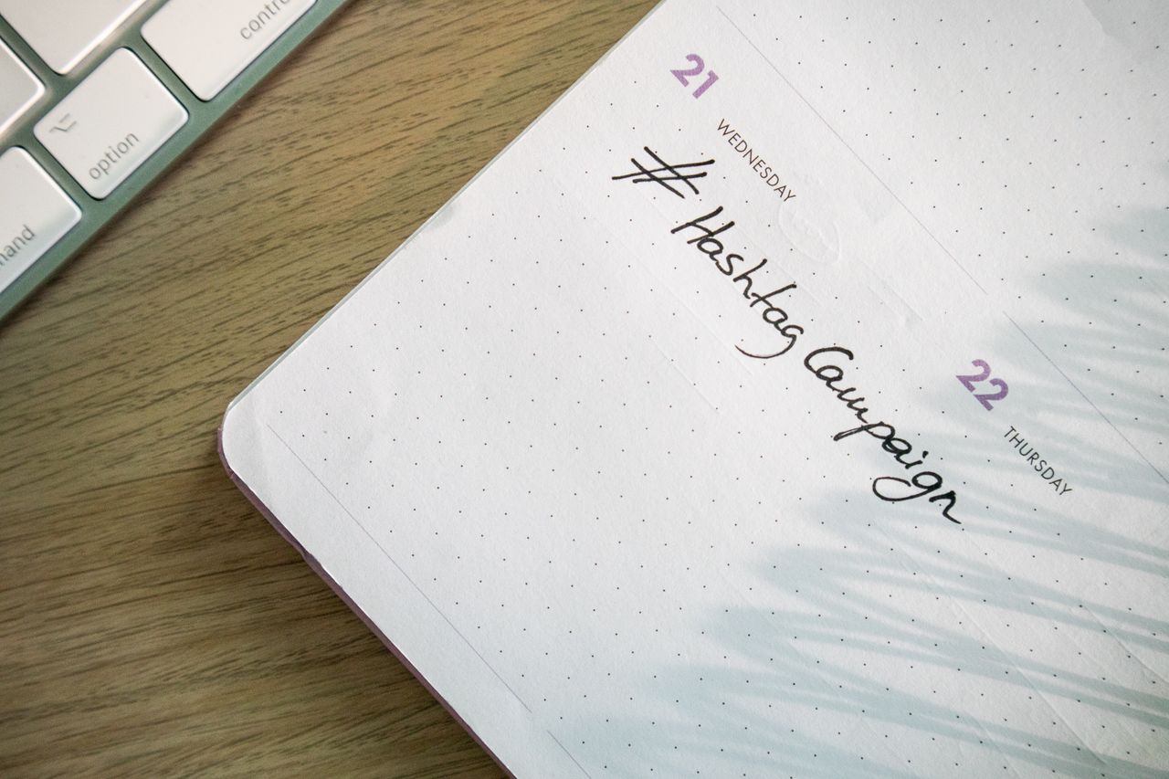 Open planner with Hashtag Campaign handwritten next to keyboard. Ideal for social media and productivity themes.